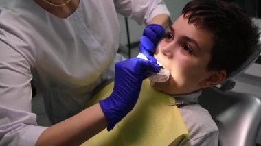 Close-up of female dentist putting on a retractor in the childs mouth, before treating teeth in dental clinic. Pediatric dentistry. Dental practice. Curing caries. Teen boy at dentists appointment