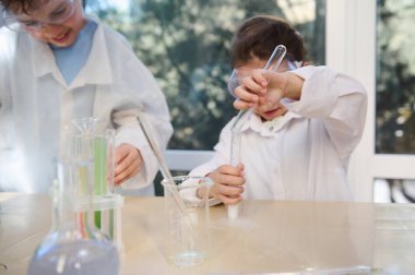 Selective focus on a little girls hands, pouring reagent from a test tube into other test tube with chemicals, during chemistry class, in the school laboratory. School, education and learning concept