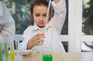 Selective focus on the hands of a smart schoolkid using graduated pipette, dripping few reagents into a test tube with chemical fluid substances. Children learning chemistry in school laboratory