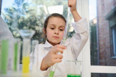 Smart little girl, primary school student using graduated pipette, dripping reagent into a test tube, while a chemical experiments, at chemistry class. Back to school on new semester of academic year