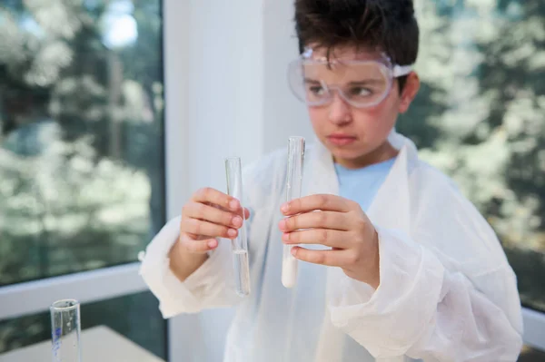 Close-up of test tubes with chemicals and reagents in the hands of a blurry schoolkid, smart teenage boy, future chemist scientist, while chemistry class in school laboratory. Science. New knowledges