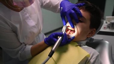 Close-up dentist hygienist doing professional teeth cleaning for a child patient in a dental clinic. Dental care and oral hygiene. Teeth whitening concept. Pediatric dentistry. Healthcare and medicine