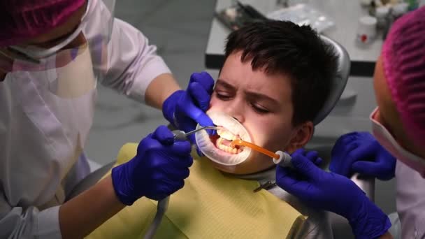 トップビュー歯科衛生士は 灌漑を使用して 10代の男の子の口を洗浄し 唾液放出器で水を収集します 小児科診療所における専門的な洗浄 歯研磨の手順 — ストック動画