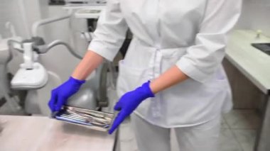 Close-up of a dental assistant or dentist hygienist carrying a metal tray with sterile dental instruments for examining and treating teeth, putting it on table in a modern white dentistry clinic