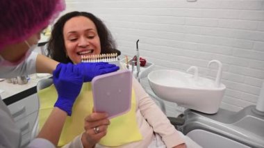 Dentist doctor placing a tooth color chart, over a beautiful smiling womans teeth, choosing the shade of veneers, according to Vita scale. The visual method of subjective perception of tooth color