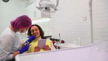 Cosmetic Dentistry. Dentist Office - multi-ethnic female patient sitting on chair before teeth checkup and teeth whitening bleaching. Doctor checks the tooth color on a comparative scale of veneers.