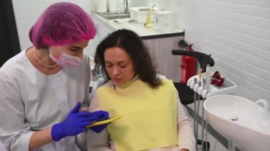Doctor shows a digital x-ray on a smartphone, explains to the patient sitting on the dentists chair the process of installing dental implants, the treatment that needs to be carried out in dentistry