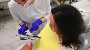 Close-up experienced confident young woman dentist doctor, explaining to her patient on dental x-ray panoramic radiography all the dental treatment that needs to do in dentistry. Dental care. Top view