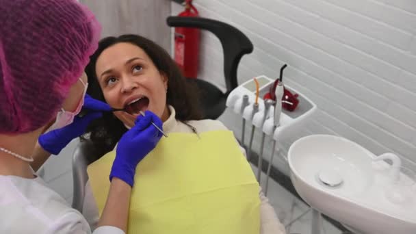 美しい多民族の女性は 歯科椅子に座って 歯科検査を受ける現代の歯科クリニックで 歯科用ミラーとスチールプローブを使用した女性医師歯科医 患者の歯を調べる — ストック動画