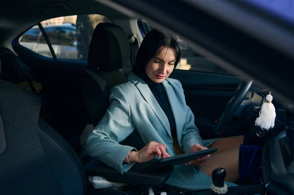 Confident Caucasian businesswoman sitting on drivers seat, using digital tablet, working on new project, telecommuting, planning meeting with colleagues. Lifestyle People Remote work business concept