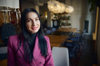 Middle-aged Caucasian stylish woman, dressed in elegant purple suit, successful business lady entrepreneur, CEO, smiling at camera, standing at her workplace in her own cozy modern restaurant