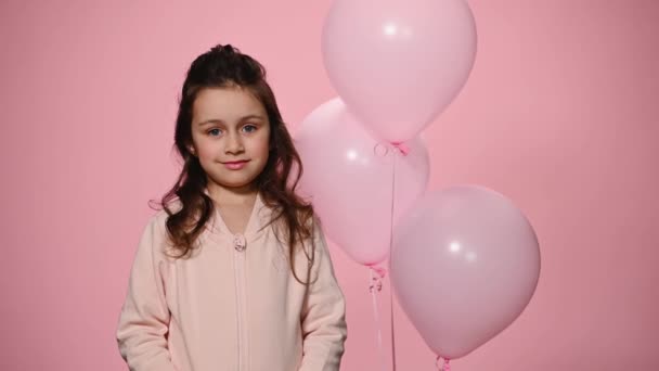 パステルピンクの服で美しい白人の小さな子供の少女の自信に満ちた肖像画は カメラを見て ピンクの色の背景に対してピンクのインフレータブル風船の近くに立っている 幸せな子供の日のコンセプト — ストック動画
