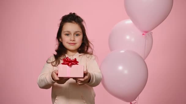 ピンクのトレーナーの美しい小さなヨーロッパの子供の女の子 ギフトボックスカメラで開催 カメラを見て笑顔 色の背景にインフレータブルヘリウムピンクのパステル風船に対してポーズ — ストック動画
