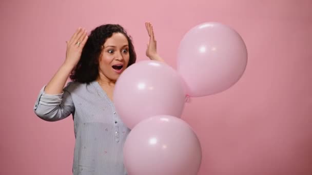 魅力的な誕生日の女の子は かなりの女性はピンクの背景に現れる膨脹可能なヘリウム気球ながら驚きと喜びを表現し 彼女の目をカバーしています 聖バレンタインまたは女性の日のコンセプト — ストック動画