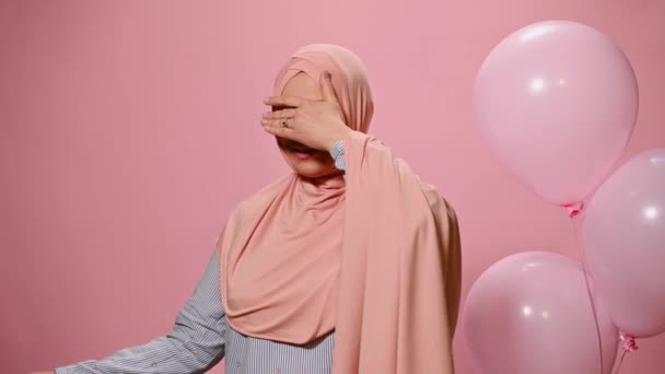 魅力的なイスラム教徒の女性は 誕生日や女性の日のための幸せな驚きとギフトボックスを受信しながら 驚きを表現し 彼女の目をカバーします カメラで笑顔 ヘリウム風船でピンク色の背景に — ストック動画