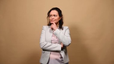 Pensive mature woman, thinking about idea and putting her index finger up, finding an excellent solution to problem, smiling a cheerful toothy smile, looking at camera, isolated over beige background