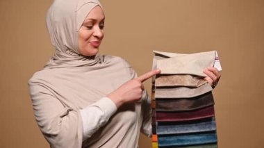 Başı bej sarısı, iç mimar ya da ev dekoratörü ile kaplı çekici Müslüman kadın, kamera örneklerine farklı renk, doku ve kalitede kanepe döşemesi, bej rengi gösteriyor.