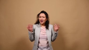 Furious anxious angry middle-Eastern woman gesturing with her hands, asking what looking at camera, expressing anger, disappointment and misunderstanding against a beige isolated background