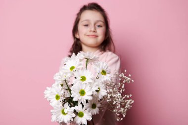 Adorable 5 years old child, lovely little girl in pink pastel clothes, smiling and holding out at camera a cute bouquet of white flowers, isolated background. Flowers as a cute present for any event