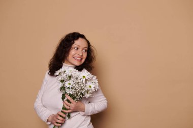 Çekici Latin Amerikalı orta yaşlı kadın portresi, günlük süveter içinde, kadınlar için bir buket taze papatya tutuyor, anneler günü, festival vesilesi, izole edilmiş krema geçmişi