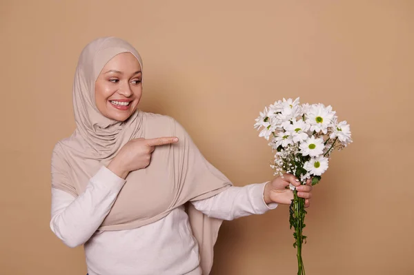 Прекрасна Близькосхідна Мусульманка Бежевому Хіджабі Посміхаючись Вказуючи Весняний Букет Білих — стокове фото
