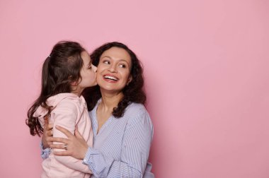 Annesini öpen, gülümseyen ve fotokopi odasına bakan beyaz bir kız. Çok ırklı güzel bir kadın mutluluğu yaşıyor. Güzel çocuğuna pembe arka planda sarılıyor.