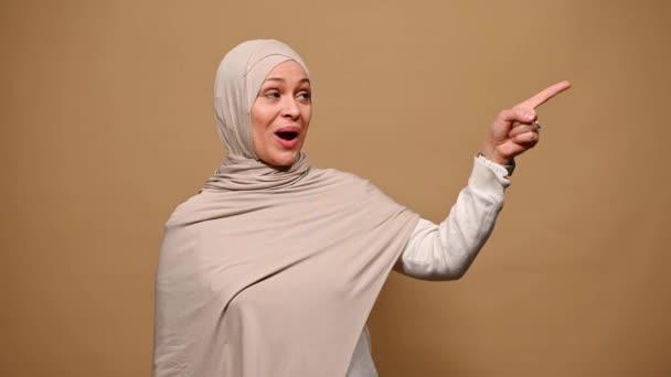 用头巾吸引阿拉伯穆斯林妇女 列举要做的事情 同时指出在米色孤立的背景下复制广告空间 微笑着看着相机 中东伊斯兰风格 — 图库视频影像