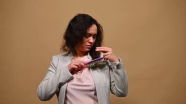 Çok ırklı orta yaşlı bir kadın saçını tarıyor. Stres yüzünden saçlarının zarar görmesinden endişe duyduğunu söylüyor. Saç problemleri - kırılgan, hasarlı, kuru ve dökülmüş saç konsepti