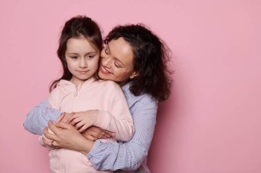 Küçük kızına arkadan sarılan mutlu, güzel bir kadın. Pembe arka plan stüdyo resminde soyutlanmış. Anne ve çocuk birlikte eğleniyor. Anneler Günü. Aile Çocukluğunu Sevmek Konsepti