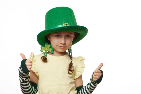 在爱尔兰 可爱的爱尔兰小女孩戴着三叶草耳环和狂欢节的绿帽 喜欢庆祝传统的节日 圣帕特里克斯节 她总是露出大拇指 被白色背景隔开 — 图库照片