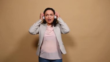 Kablosuz kulaklıklı, müzik için özgürce hareket eden, izole edilmiş bej arka planda dans eden neşeli orta yaşlı bir kadın. İnsanlar Hobi Eğlencesi Yaşam Tarzı Eğlencesi Etkinliği
