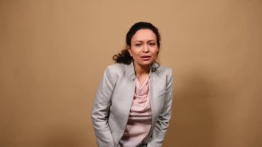 Güzel bir kadın dikkatlice uzaklığa bakıyor, seviniyor, mutluluk ve olumlu duyguları ifade ediyor, avuçlarını bir arada tutuyor, umut dolu bir şekilde bej arka planda kameraya bakıyor.