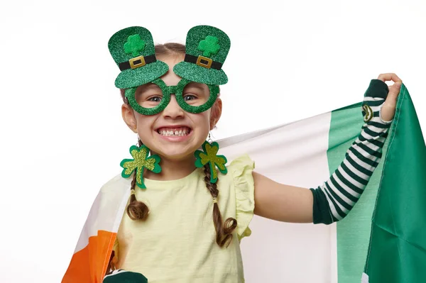 可爱的小女孩 身穿时髦的嘉年华服装 头戴三叶草耳环 参加圣帕克斯节的庆祝活动 面带微笑 脸上挂着爱尔兰国旗 背景是孤立的白色 — 图库照片