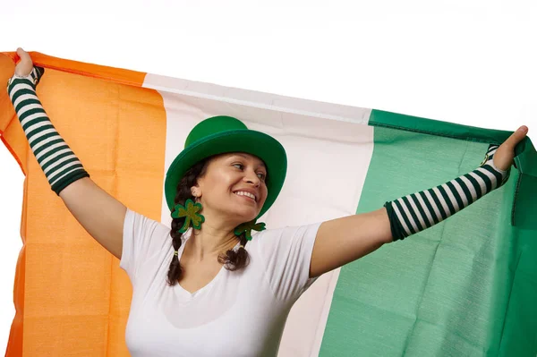 迷人的爱尔兰女性头戴绿色的圣帕克斯帽 头戴三叶草耳环 手持爱尔兰国旗 流露出快乐而积极的情绪 在白色的背景上被隔绝 有免费的广告空间 — 图库照片