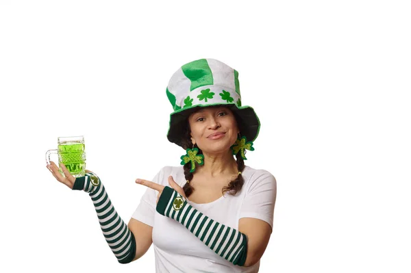 クローバーの葉や縞模様の手袋とカーニバルの帽子の美しい多民族の女性は 緑のビールのマグカップを示し カメラを見て笑顔 隔離された白い背景 聖パトリックの日のコンセプト — ストック写真