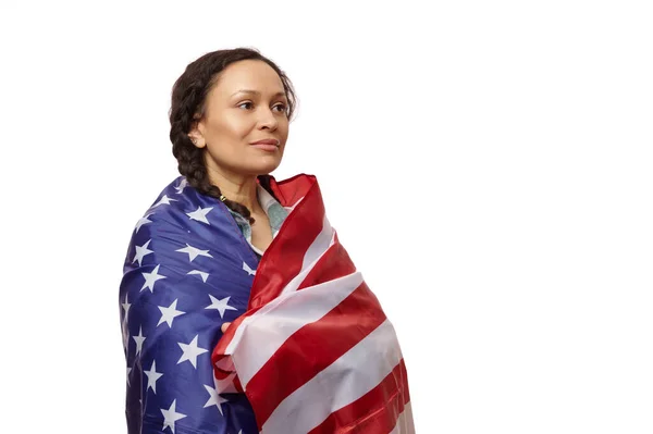 stock image Proud multinational woman wrapped in the flag of the United States of America, looking away on an isolated white background, proud to be an American citizen. Copy ad space. July 4th. Independence Day