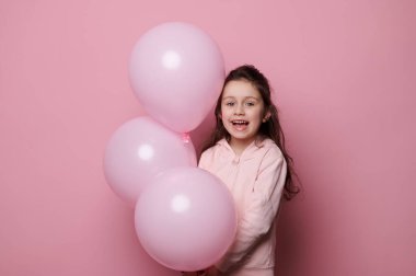 Kafkas güzeli küçük bir çocuk, pembe elbiseli doğum günü kızı, kameraya gülümseyen, pembe pastel helyum balonları ile poz veren, pembe renkli arka planda fotokopi alanı olan