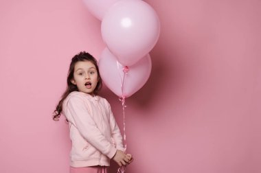 Sevimli küçük kız elinde bir demet pembe pastel balonla pembe arka planda izole edilmiş kameraya güvenle bakıyor. Duygular. Çocuklar işte. Uluslararası Çocuk Günü konsepti