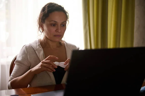 Multitasking woman, entrepreneur sitting at laptop, feeling exhausted and tired, using medicated eye drops to relieve dry eyes and digital eye strain. Health care and medicine. Ophthalmic concept