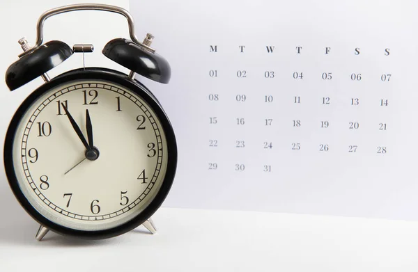 Close-up of a black retro alarm clock and white clean calendar, isolated over white color background with copy ad space. Busy work reminder, annual leave, project deadline or special event day concept