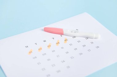 Seçici odaklanma. Hamilelik mürekkep testi ve mavi arkaplanda son adet tarihlerinin yazılı olduğu bir takvim. Kadın sağlığı. Yumurtlama tarihi hesaplaması. Hamilelik ve annelik planlama