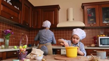 Anne ve kızı ev mutfağında birlikte yemek yapıyor. Aşçı gibi giyinmiş sevimli küçük bir kız çocuğu. Fırıncı paskalya pastası hamuru yoğuruyor. Geleneksel Hıristiyanlar bayramı. İlkbahar