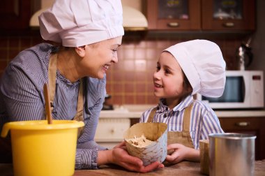 Sevgi dolu bir anne ve güzel bir çocuk, şefler gibi giyinmiş sevimli bir kız, birbirlerine bakıp gülümseyen, hamur ile kağıt pişirme tabağını tutan Paskalya pastası panettone 'u hazırlayan