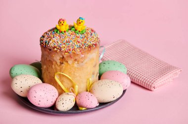 Paskalya pastası, panettone ve donanma tabağında renkli yumurtalar, kırmızı kareli peçetenin yanında, pembe renkli arka planda izole edilmiş. İlkbaharda Ortodoks ve Katolik Paskalyasını kutluyoruz. Dini bayram