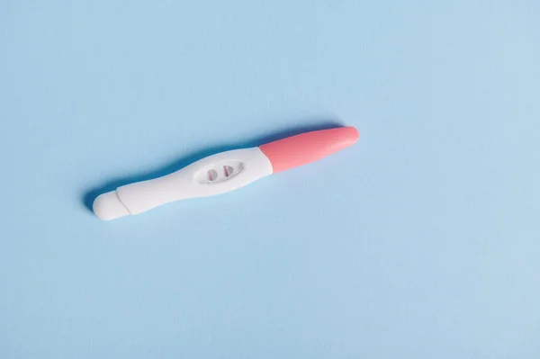 View from above of a positive pregnancy test over blue background with free advertising space for text. Womens health and fertility concept. Rapid diagnosis of pregnancy at home. Gynecology. Medicine