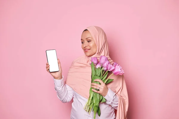 Щаслива Вагітна Арабська Мусульманка Рожевому Хіджабі Букетом Тюльпанів Дивлячись Смартфон — стокове фото