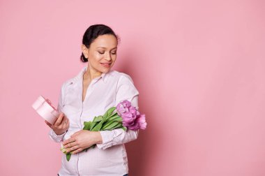 Mutlu, orta yaşlı, Afrika kökenli hamile bir kadın, mutlu bir hediye ve bir buket lale ile poz veriyor, izole edilmiş pembe arka plan. Uzayı kopyala Sevgililer Günü. Uluslararası Kadınlar ve Anneler Günü