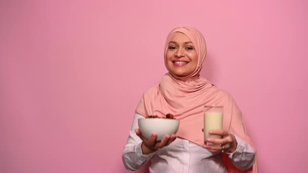 有选择的重点 碗里放着新鲜的甜枣子和一杯牛奶 手里拿着被埋葬的阿拉伯穆斯林美女粉红头巾 在斋月禁食后 在镜头前分发健康健康的早餐 — 图库视频影像