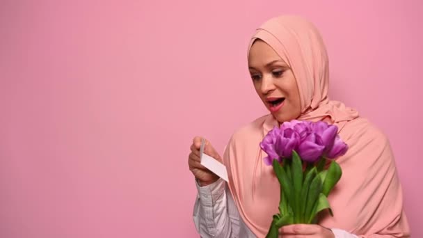 在特写中 穿着粉色头巾的优雅优雅的穆斯林女性 在收到带有神秘信封的郁金香花束时 她表现出惊奇和快乐 微笑和感动 — 图库视频影像