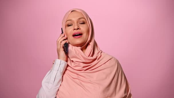 분홍색 히잡으로 얼굴을 아름다운 이슬람 전화로 말하고 부드럽게 배경에 — 비디오